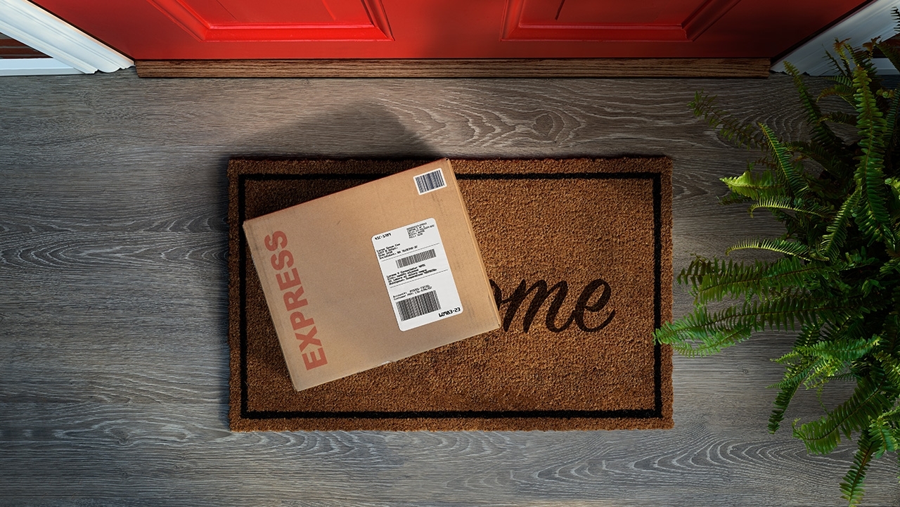 An express courier delivery box rests on a welcome mat outside a front door. (Overhead view.) 